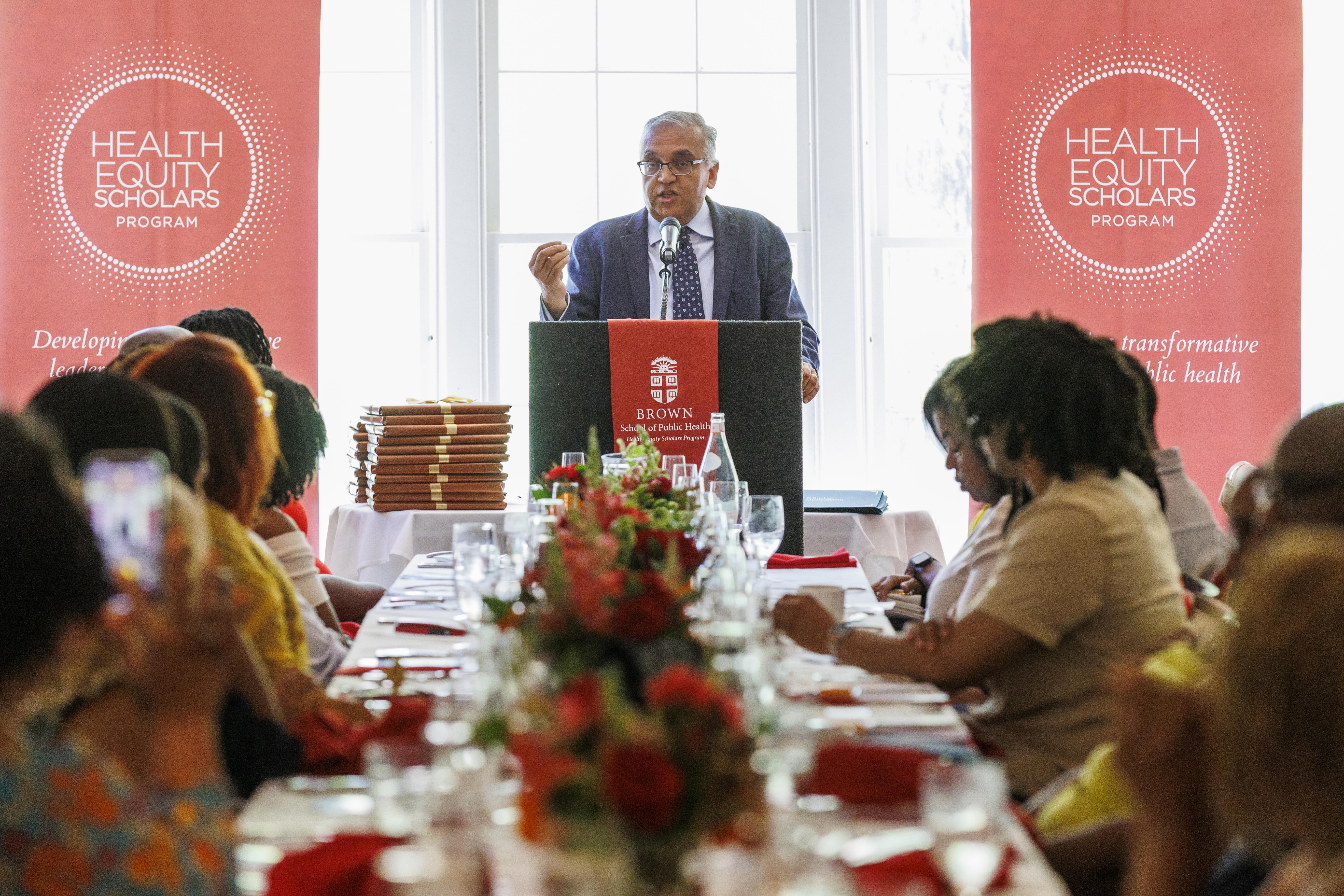 Dean Jha speaking at a podium to table of students
